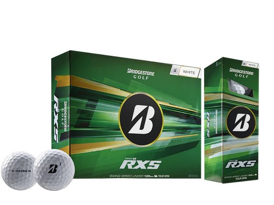 Zwei glänzende, weiße Bridgestone Tour B RXS Golfbälle mit schwarzem „B“-Logo liegen vorn. Im Hintergrund sind zwei grüne Verpackungen zu sehen: eine größere Schachtel für ein Dutzend und eine schmale, aufrechte.